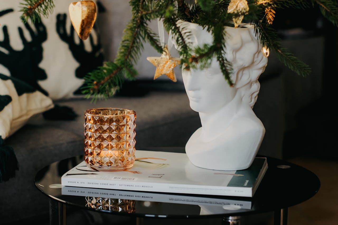 A cozy interior featuring a candle and a decorative sculpture under a Christmas tree branch.