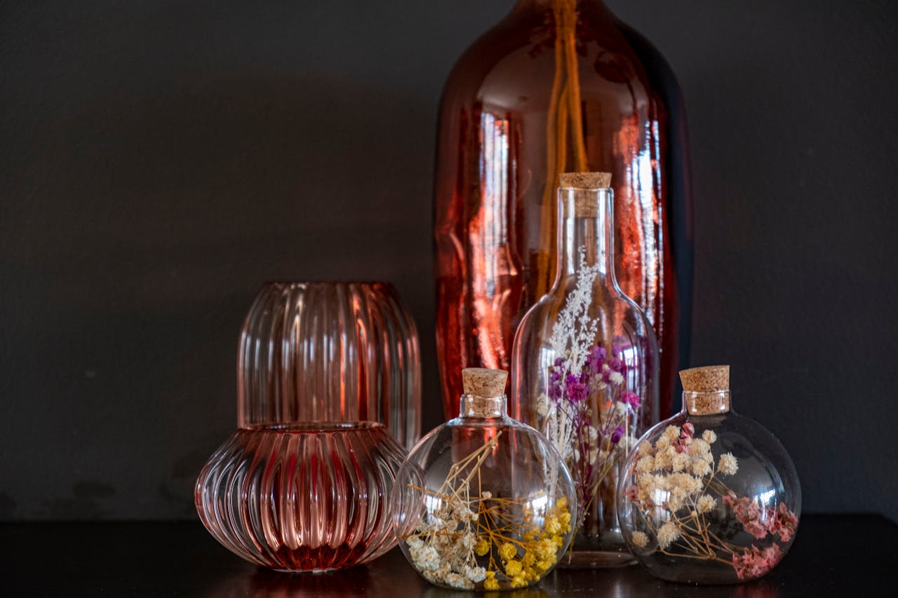 Artistic composition of glass vases with colorful dried flowers against a dark background.